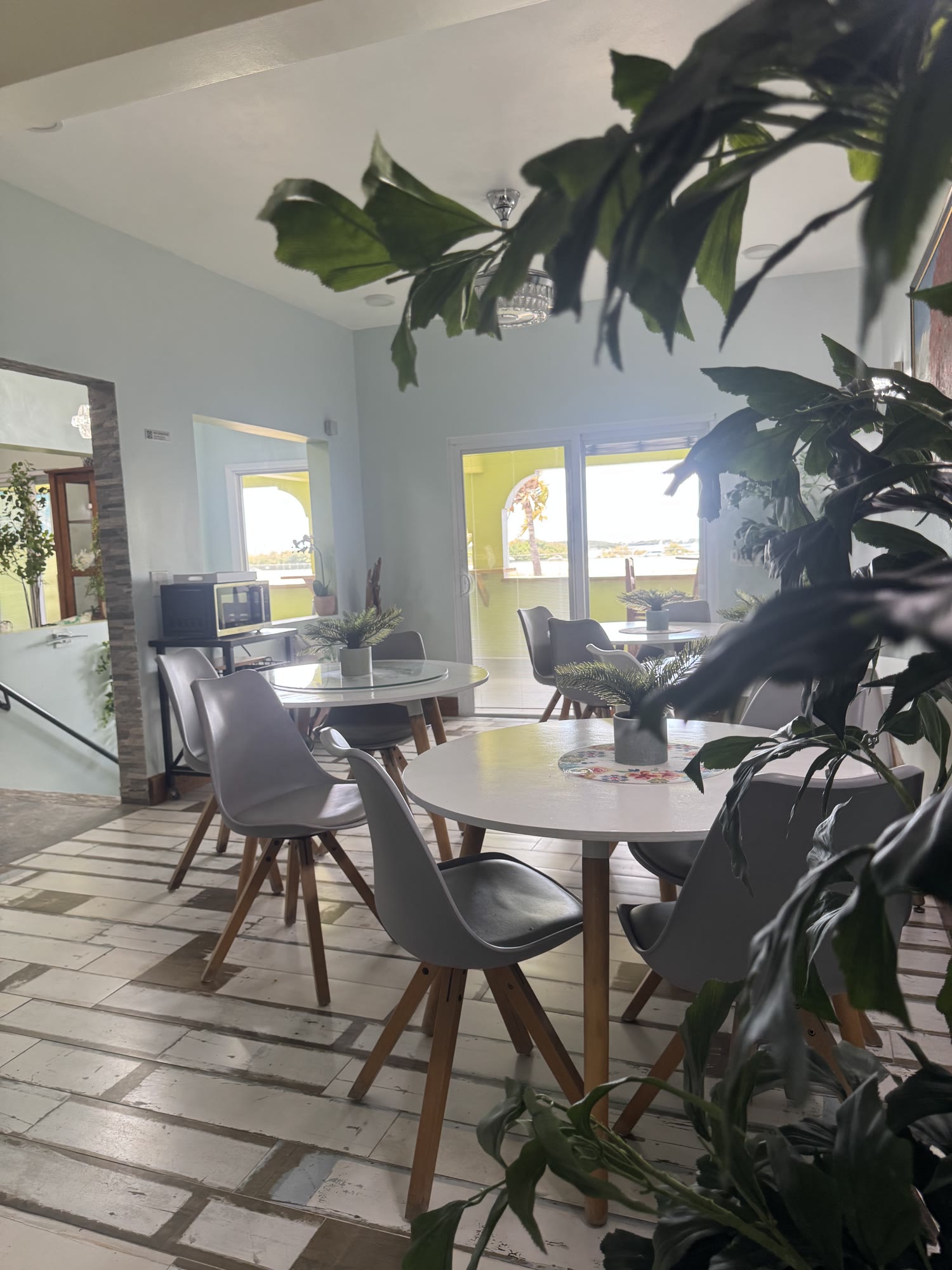 The bright open social room at BethsAida, round tables and grey chairs under a crystal chandelier with daylight windows