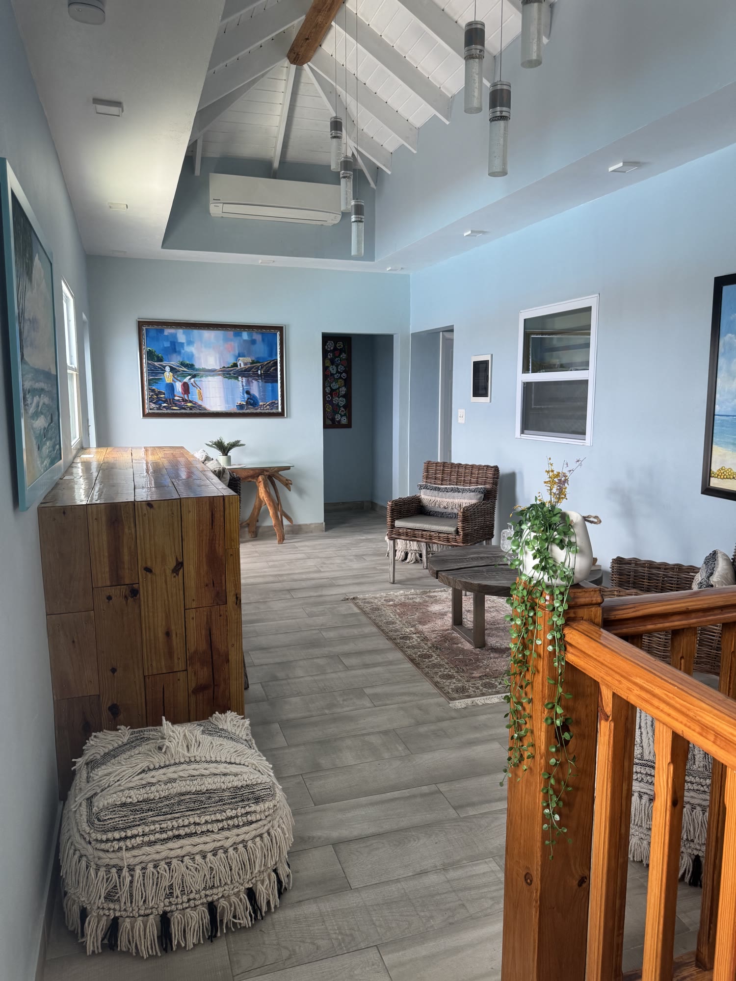 The upstairs landing lounge at BethsAida — a wicker armchair, reclaimed-wood console and coastal art under a vaulted white ceiling