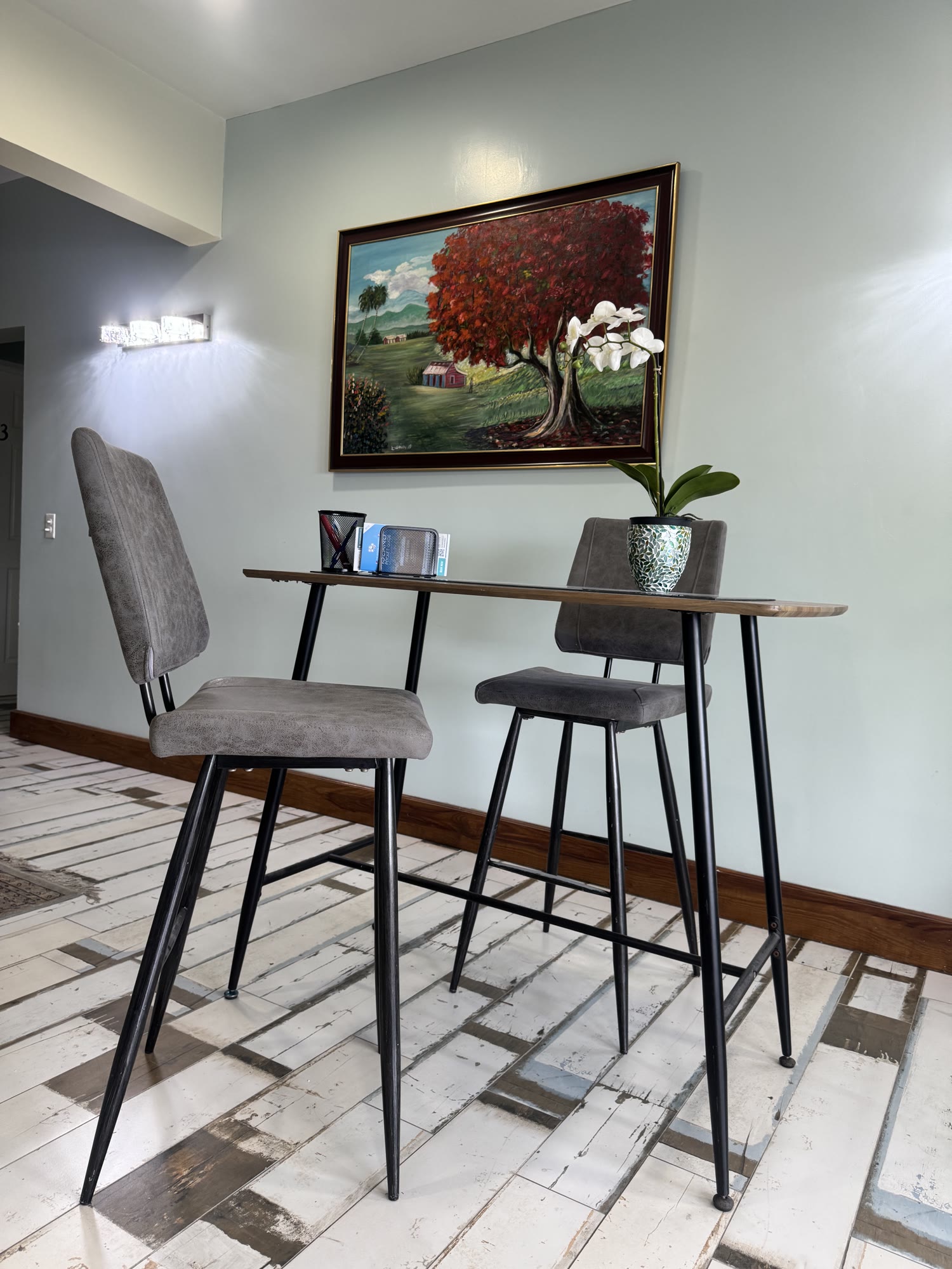 A bar-height counter with grey stools and a flamboyant-tree painting at BethsAida — a stand-up perch for working