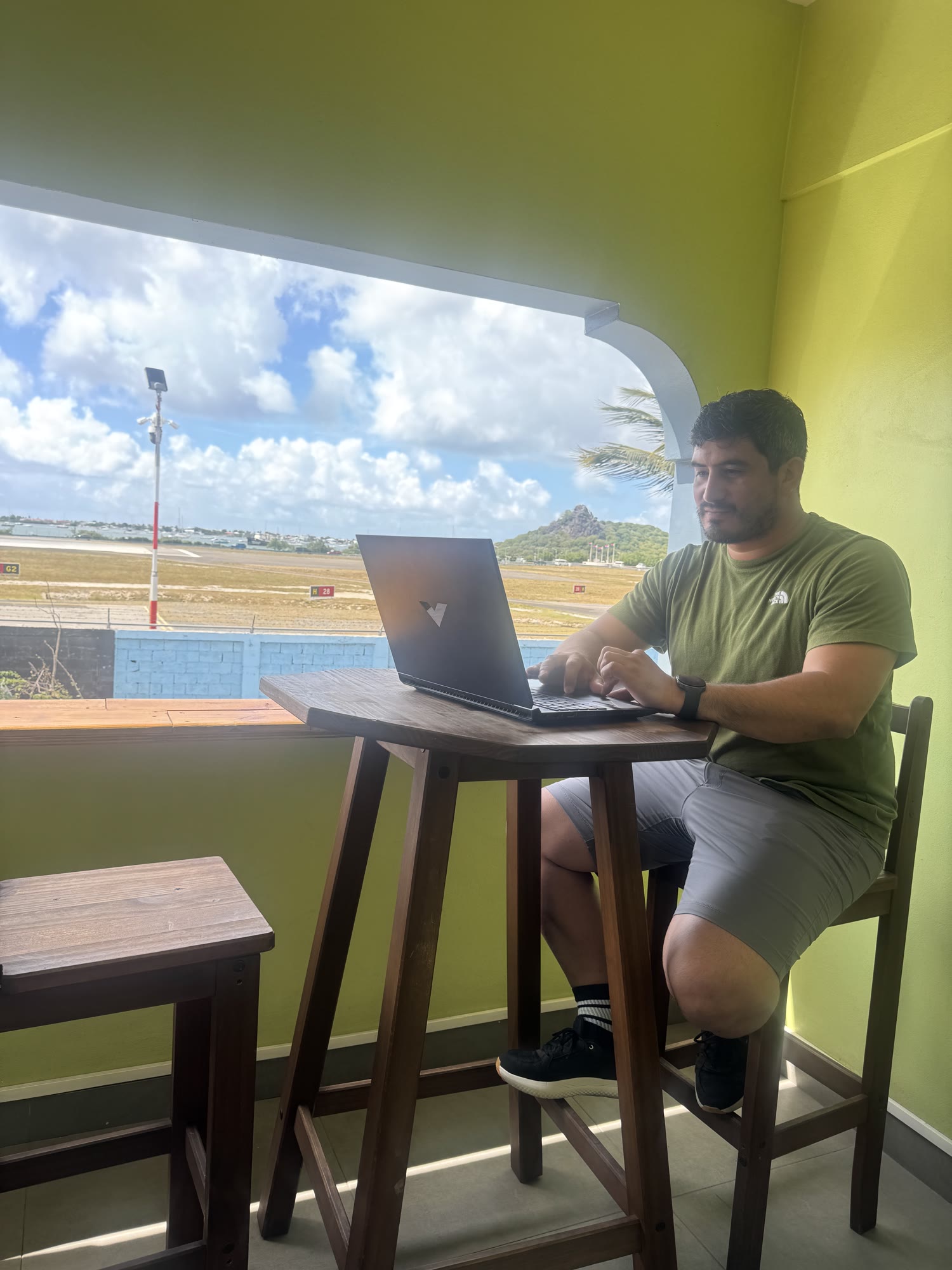 A guest working on a laptop at the counter, the SXM runway and green hills beyond